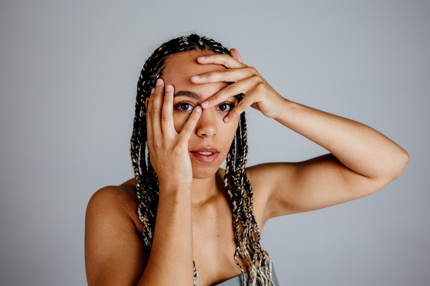 Woman is holding her hands near her face and has braided long hair
